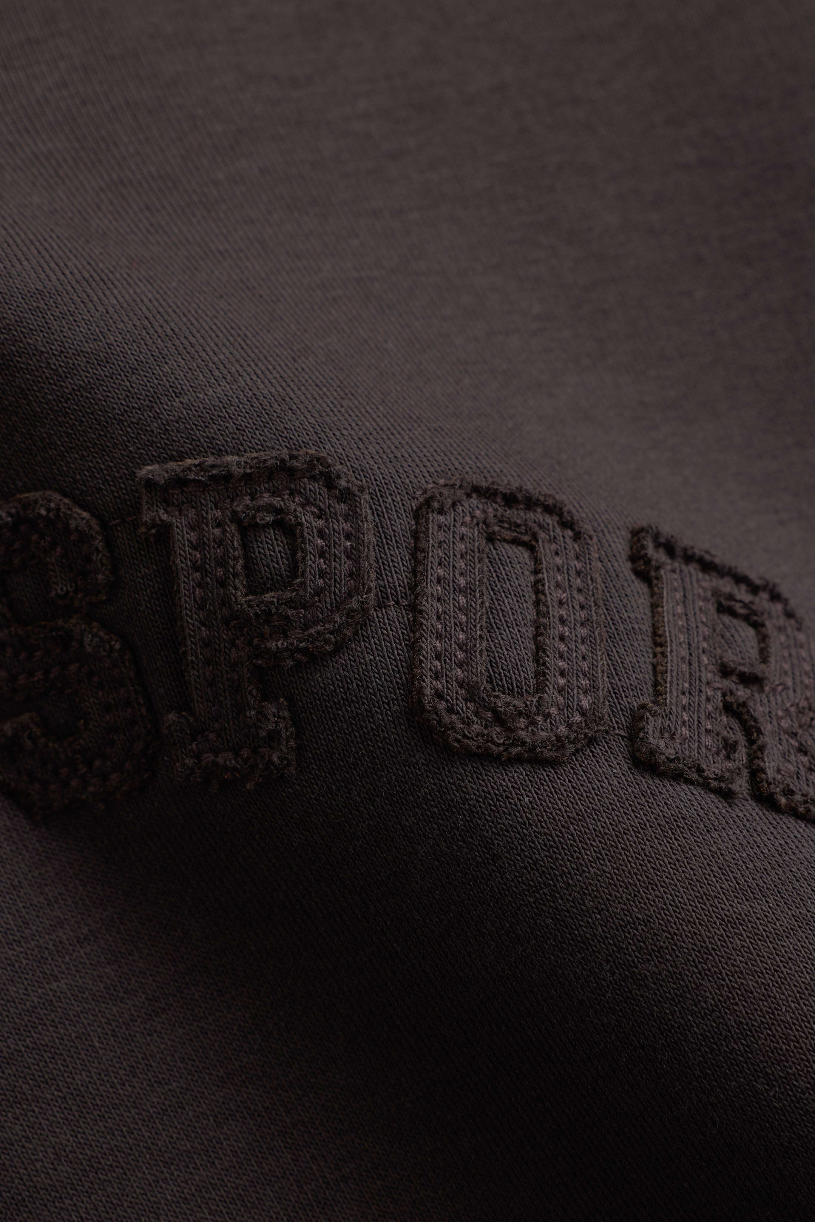 Close-up of embroidered tonal lettering on an espresso CASPARA CS hoodie.